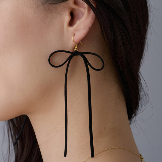 A close-up side view of a model's ear wearing a black bow-shaped dangling earring with a small gold stud at the top.