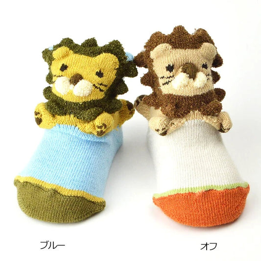 Color variation of baby socks with plush lion faces on the toes, shown side by side on a white background. One pair is light blue with an olive green toe, and the other is white with an orange toe.