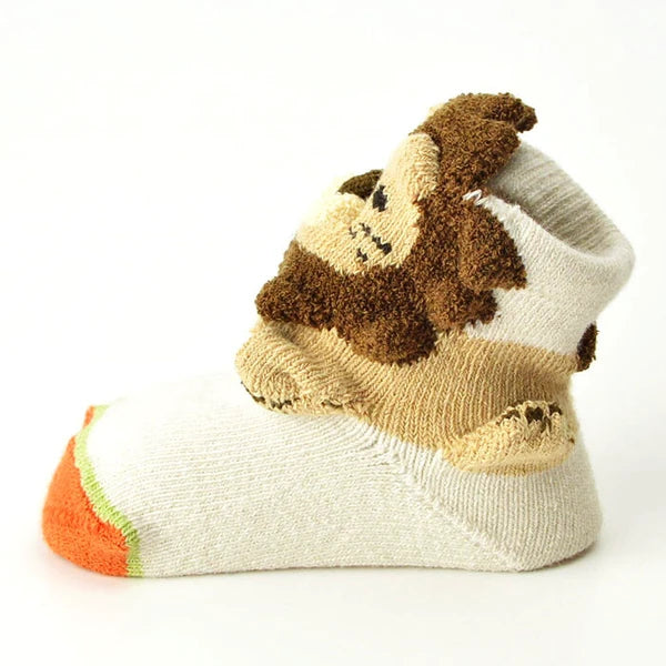 A baby bootie sock featuring a plush, raised monkey face design in brown and beige, with an orange and green striped toe, shown on a white background.