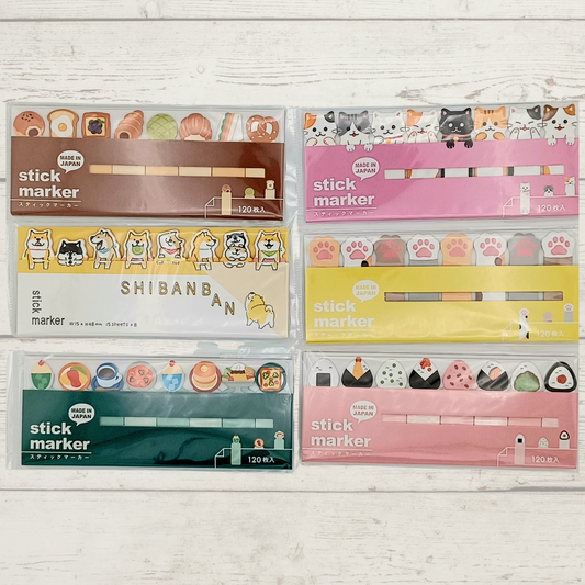 Six packs of cute-themed stick markers arranged in a 2x3 grid on a white wood background. The packs feature various designs including Shibanai, cats, dogs, paw prints, and food illustrations in brown, pink, yellow, and green packaging.